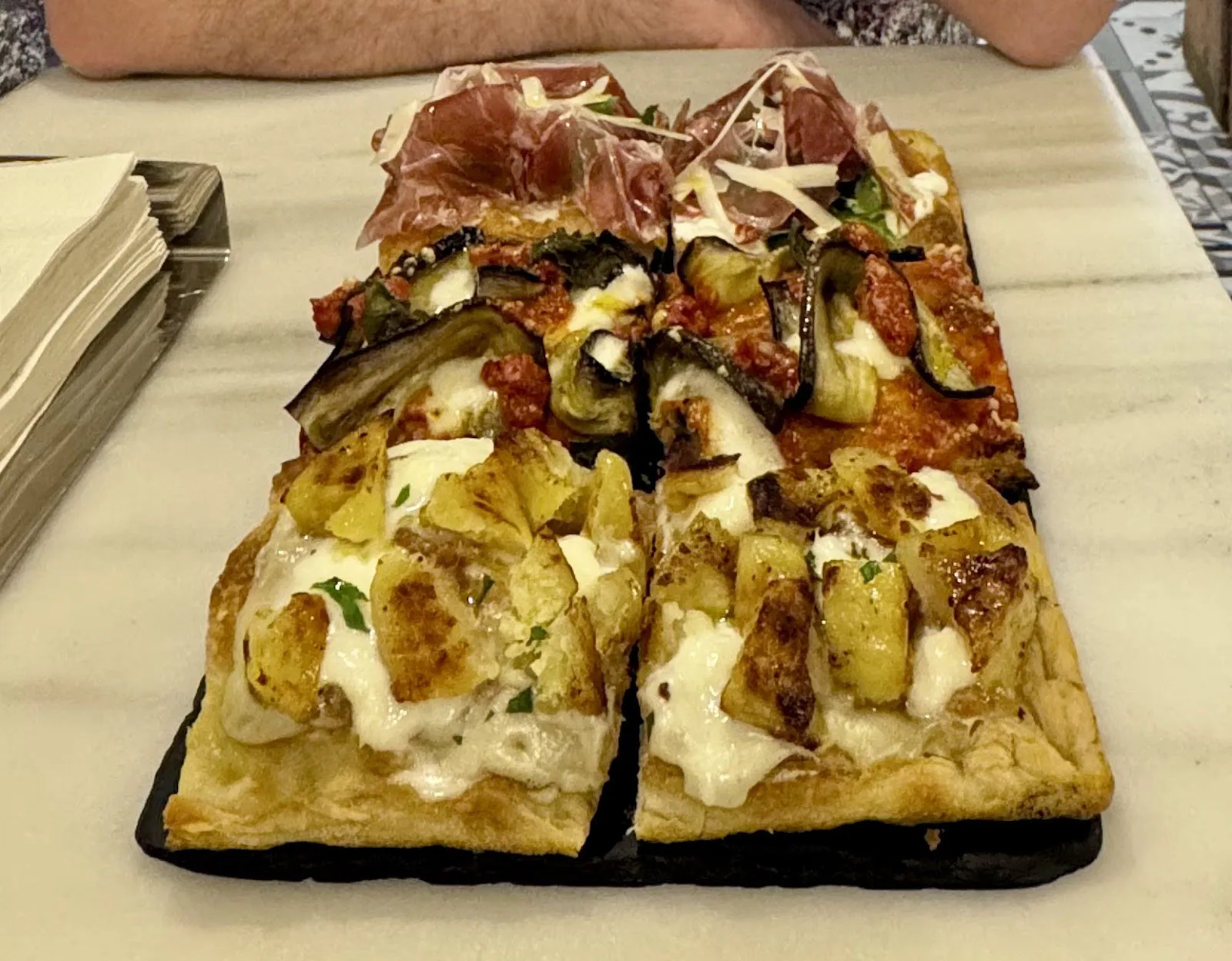 Porcions de pizza in teglia sobre una pissarra, amb pernil curat i amb albergínia, entre d'altres