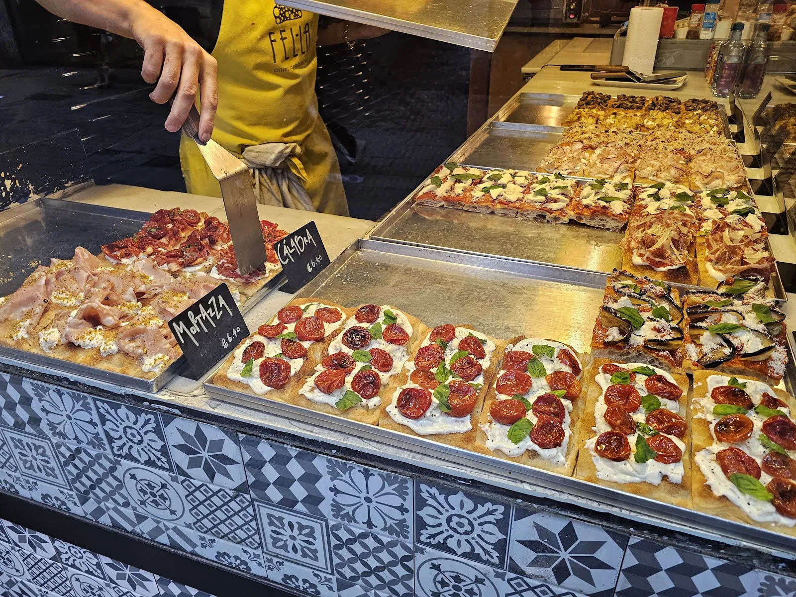 El taulell de Fella amb safates de pizza a talls, entre elles la Mortazza, amb mortadel·la, burrata i pistatxo